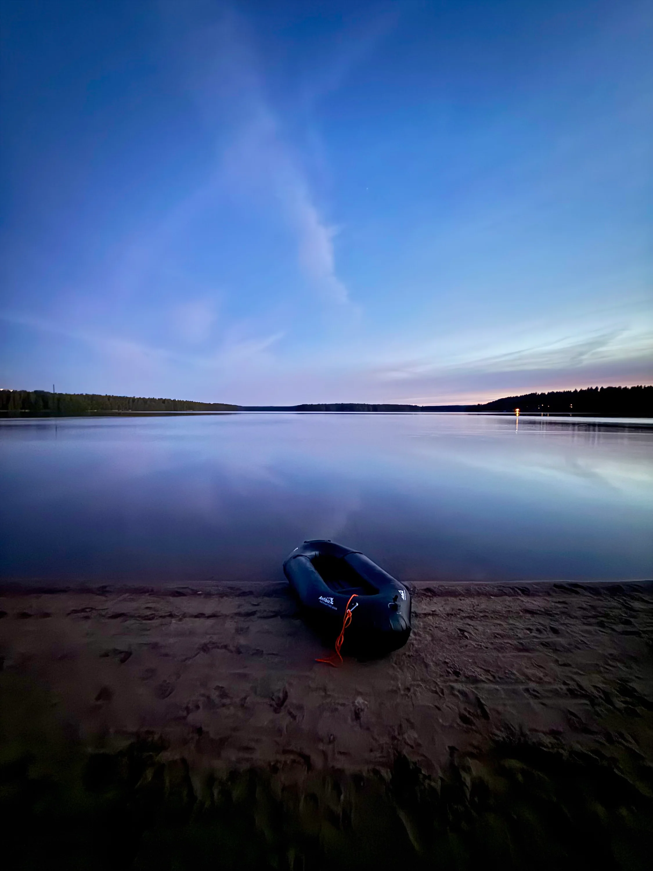 A packraft on a quiet beach beside a Finnish lake at dusk